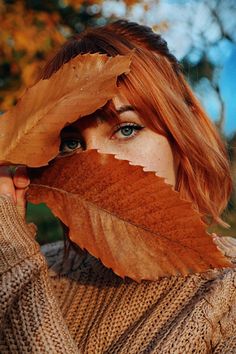 a woman with red hair and blue eyes is holding up a leaf to her face