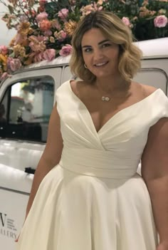 a woman in a white dress standing next to a car with flowers on the back