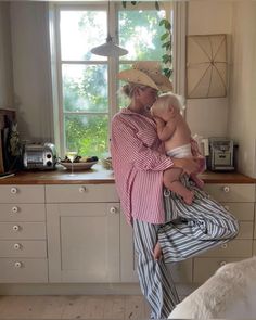 a woman holding a baby in her arms while standing next to a kitchen counter top