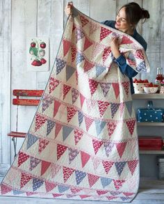 a woman holding up a quilt in front of a wooden wall