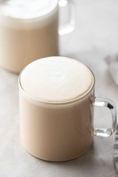 two mugs filled with liquid sitting on top of a white cloth covered tablecloth