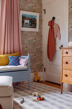 a child's bedroom with pink and blue wallpaper, striped rug, wooden dresser and toy chest