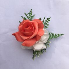 an orange rose and white flowers are on a table top with green leaves in the corner