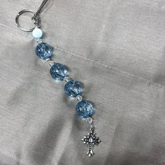 a blue beaded keychain with a silver cross charm hanging from it's side