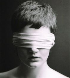 a black and white photo of a woman with blind folded over her eyes, looking at the camera