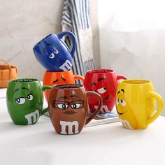 five different colored mugs sitting on top of a white table next to each other