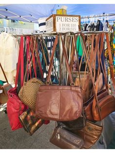 several purses are hanging on a rack at an outdoor market