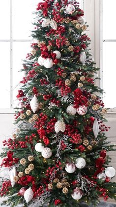 a decorated christmas tree with red and white ornaments on the top, in front of a window