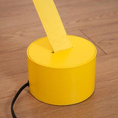 a yellow table lamp sitting on top of a wooden floor next to a black cord