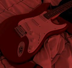 a red electric guitar laying on top of a bed