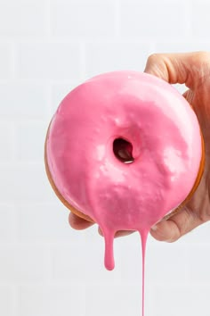 a hand holding a pink donut with icing on it's side and dripping from the top