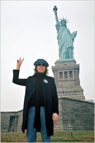 a woman standing in front of the statue of liberty with her hand up to the sky