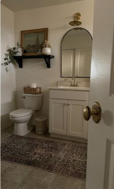 a white toilet sitting next to a sink in a bathroom under a mirror and shelf