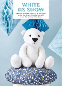 a white teddy bear sitting on top of a blue pillow with an origami background