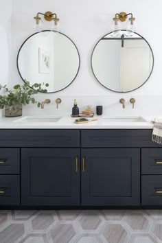 two round mirrors are above the double sink vanity in this bathroom with geometric tile flooring