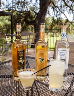 three bottles of alcohol sitting on top of a table next to a glass filled with liquid