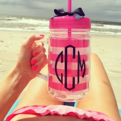 a woman laying on top of a beach holding a pink and white striped mason jar