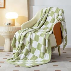 a green and white checkered blanket sitting on top of a chair next to a lamp