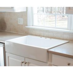 a white kitchen sink sitting under a window next to a counter top and cupboards