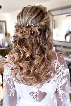 the back of a woman's head with long curly hair and flowers in her hair