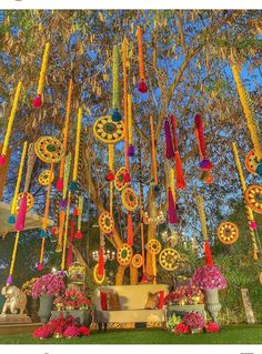 a bunch of colorful decorations hanging from a tree in front of some flowers and trees