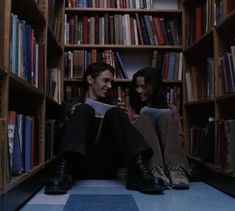 two people sitting on the floor in front of bookshelves