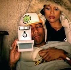 a man laying in bed next to a woman wearing a hat and holding an old camera