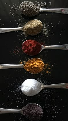 five spoons filled with different colored powdered food on top of a black surface