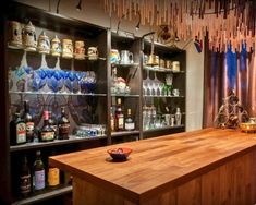 a wooden counter topped with lots of bottles next to a shelf filled with wine glasses