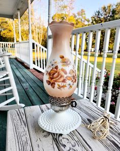 a vase sitting on top of a wooden table next to a white chair and railing