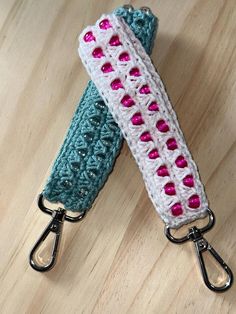 two crocheted key fobs with pink and green hearts on them sitting on a wooden surface