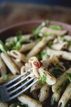 a bowl filled with pasta and vegetables on top of a wooden table next to a fork