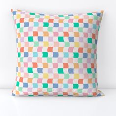 a multicolored square pillow sitting on top of a white table next to a wall