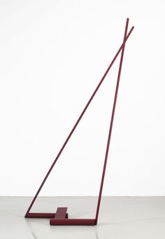 a red sculpture sitting on top of a white floor next to a tall pole with two long sticks sticking out of it