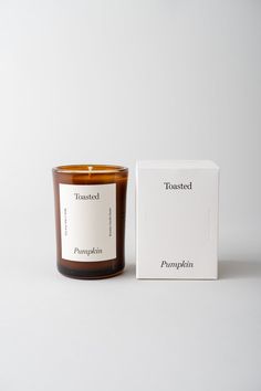 a candle sitting next to a box on a white surface with the words toasted pumpkin printed on it