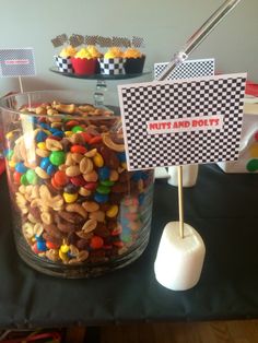 a table topped with a glass filled with lots of candy and nuts next to a sign