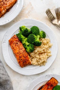 two plates with salmon, broccoli and rice on them next to silverware