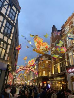 many people are walking down the street with kites in the air above them,