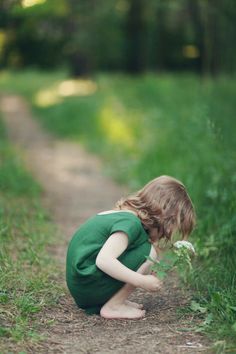 a little boy kneeling down on the side of a dirt road next to a flower