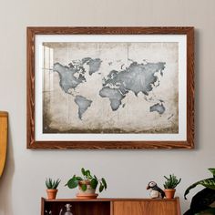 an old world map hangs on the wall above a wooden cabinet with potted plants