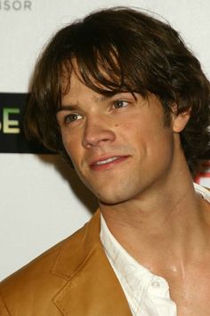 a man in a brown leather jacket posing for the camera with his hair pulled back