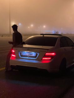 a man sitting on the back of a white car in front of a foggy street