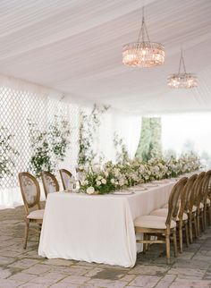 a table set up with white flowers and greenery on the tables for an outdoor wedding reception