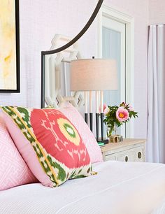 a bed with pink and green pillows on top of it next to a white dresser