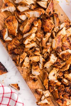 sliced chicken on a wooden cutting board next to a red and white checkered napkin