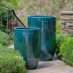 two large blue vases sitting next to each other on a sidewalk in front of bushes