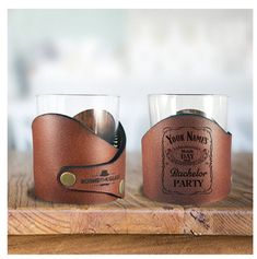 two glasses sitting on top of a wooden table next to each other and one has a leather band around it