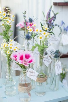 several glass vases with flowers in them are on a blue table cloth and have tags attached to them