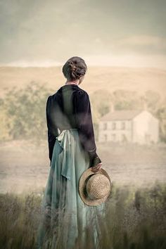 a woman standing in a field with her back to the camera, holding a straw hat