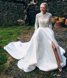 a woman in a white wedding dress sitting on the ground next to a stone wall